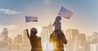 © kieferpix - Patriotic man, woman, and child waving American flags in the air on city sunrise background