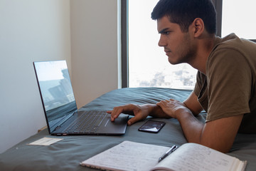 Poster - Young male studying with a laptop while lying on the bed