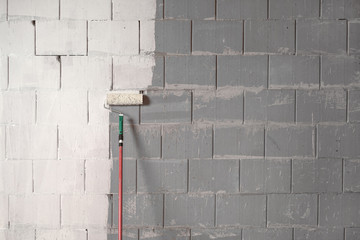 Roller is painting a rough wall of grey stones with white paint, background concept for constriction, building and renovation, copy space