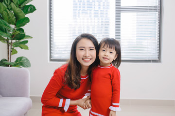 Wall Mural - Portrait of young Asian mom hugging her daughter at home.