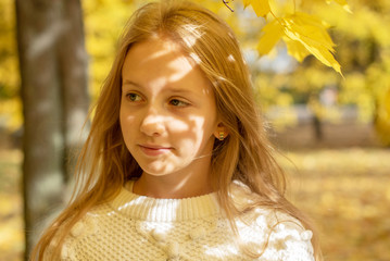 beautiful blonde teen girl walking in an autumn Park with maple trees