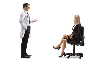 Wall Mural - Male doctor standing and talking to a businesswoman seated in a chair