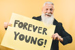 Happy youthful senior feeling forever young - Hipster mature man giving message with yellow banner - Elderly people lifestyle and positive emotions concept
