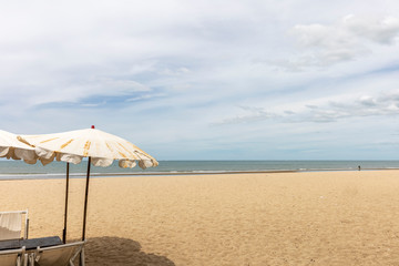 Beach umbrella at foreground. Scenic view of empty tropical sandy and peaceful beach under cloudy blue sky with light turquoise waves.