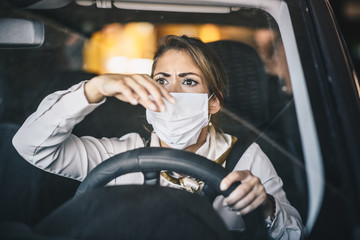 A young woman drives a car with a mask on her face, stressed due to traffic jams, life during a pandemic caused by a virus