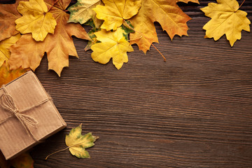 Wall Mural - cardboard box tied with string on a bow on a wooden background in autumn leaves, holiday gift on Thanksgiving Hellouin. view from the top. copy space