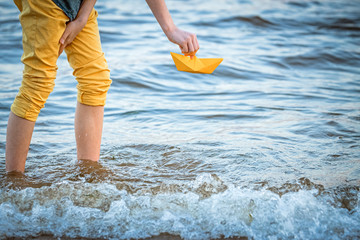 Wall Mural - a boy launches a boat made of yellow paper into the sea, a symbol of travel, summer holidays, dreams of a cruise