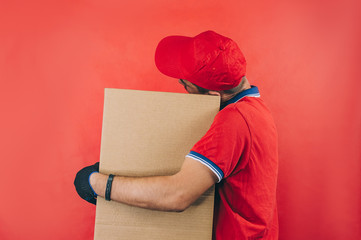 Guy with a cardboard box in his hands. Delivery service concept on red background.