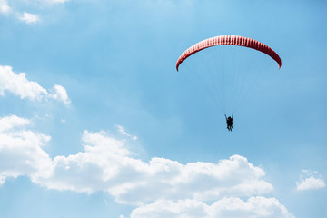 red Paraglider flying into the sky with clouds on a sunny day