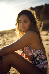 Poster - Vertical shot of a female in a swimsuit sitting on beach sands on background of sun rays