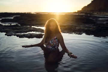 Poster - Beautiful female with a swimsuit posing in the water on background of a sunset