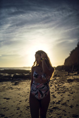 Sticker - Vertical shot of a female in swimsuit walking on a shore during sunset