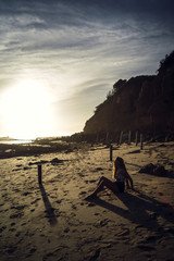 Poster - Vertical shot of a female in swimsuit sitting on sands during sunset