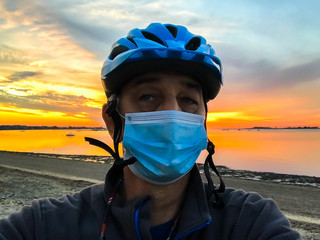 Biker with protective mask and sunrise on beach