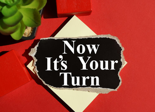it is your turn. text on black paper on a red background, near red cubes and plants close-up, white font
