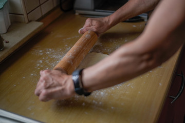 Wall Mural - Selective focus shot of a female roll out the dough with a wooden rolling pin in the kitchen