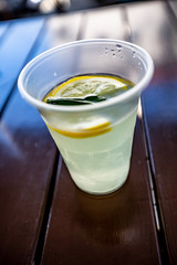 Lemonade with mint and lemon in a plastic disposable cup on a wooden table outside in summer. Vertical orientation. High quality photo