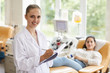 © AnnaStills - Portrait of female doctor smiling at camera while examining patient at the hospital