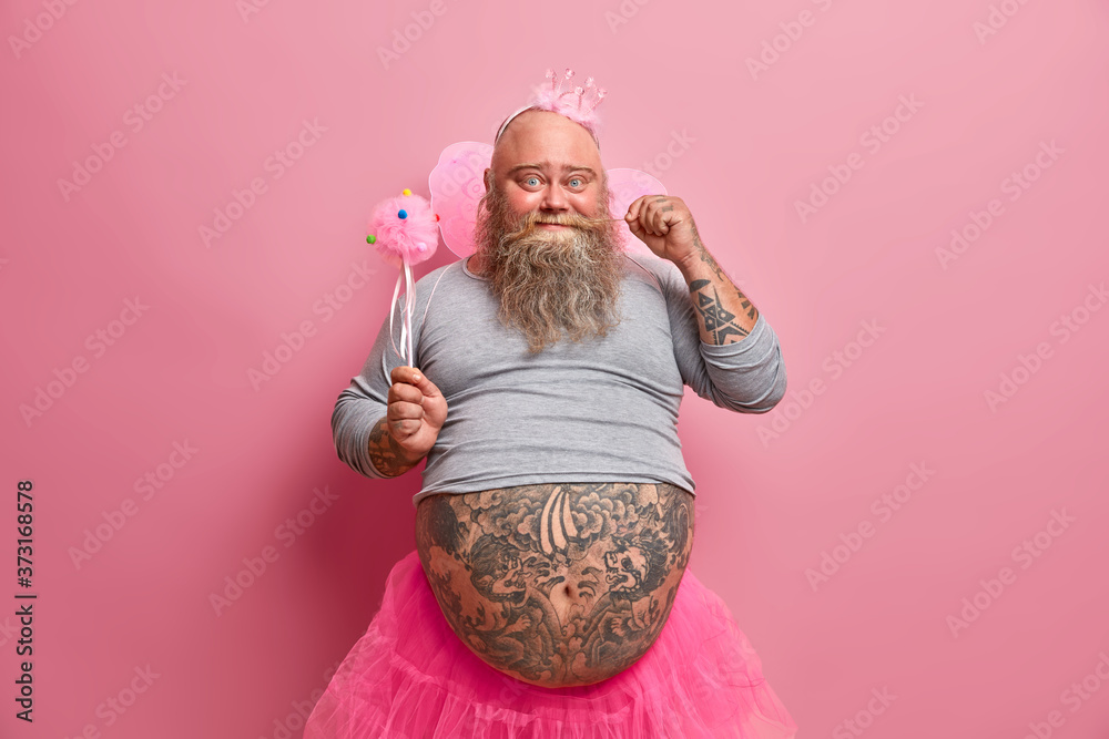 Handsome positive fat man curls mustache, has fun on party, feels like real princess, wears crown, wings, organises baby shower for her newborn daughter. Beared fatso fairy has childish mood - obrazy, fototapety, plakaty 