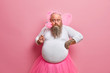 © wayhome.studio  - Obese bearded man dresses for hallooween party, plays fairy with magic wand, looks surprisingly at camera, wears wings and crown on bald head, being at childrens holiday. Funny dad princess.