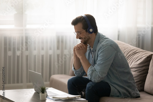 Cuadros en Lienzo Smiling young Caucasian man in wireless headphones sit on couch at home watch we