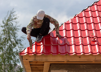 Workers install red metal tiles on the roof