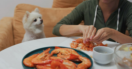 Woman eat shrimp with her dog sit aside at home