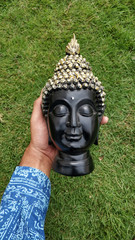 Poster - Vertical shot of a hand holding a Buddha head statue in front of the green grass