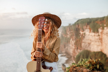 Wall Mural - Face of a girl looking at the camra and smiling, eye is covered with the neck of the guitar. She was playing guitar near the sea at  sunny summer day.