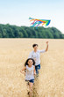 © sergo321 - Mother and daughter run in a wheat field with a kite in the summer. Well-planned and active weekend. Happy childhood.