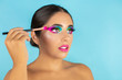 © Irene - Beauty portrait of female model with vivid makeup and brush on blue background.
