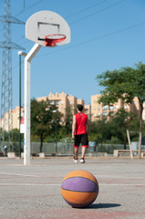 Wall Mural - Vertical selective focus shot of a basketball in a court with the male player walking near the ring