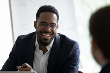 Pleasant business conversation. Positive afro american executive consulting customer, happy dark-skinned employee talking to colleague at workplace, smiling reporter interviewing a person, close up