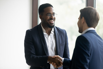 Poster - Satisfied african insurer, manager or consultant shaking hand to european customer, happy diverse male business partners completing a deal with handshaking, two colleagues employees meeting in office