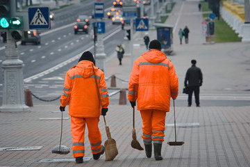 Wall Mural - Workers sweeping pavement with broom. Workers walking with broom and scoop in hands andd sweep street. Municipal worker in uniform with broomstick and scoop for garbage, cleaning service