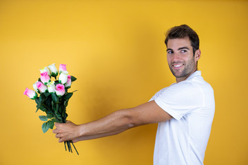 young handsome man standing over yellow insolated background smiling sending flowers