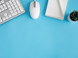 Poster - top view of office desk table with notebook, plastic plant, smartphone and keyboard on blue table background, graphic designer, Creative Designer concept.