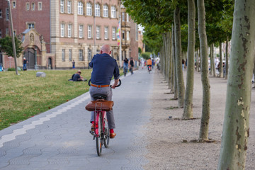 Wall Mural - Office man, Male cyclist ride bicycle on bicycle lane on promenade riverside of Rhein River in Düsseldorf, Germany. Cycling friendly city in Europe. Eco friendly mobility transportation.