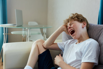 sleepy boy sit on sofa at home. has no enough sleep in the morning, alone. yawning