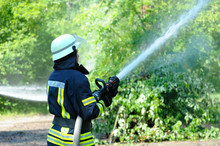 Fireman In Protective Ensemble Fighting Fire Watering Forest With Syringe