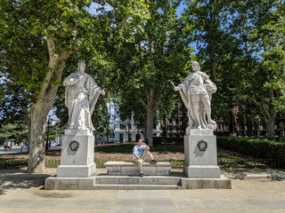 Poster - Person sitting between two statues at the Plaza de Oriente, Madrid, Spain