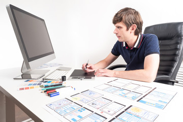 Poster - Mobile application designer. Man is working on application design. Designer works with a graphic tablet for drawing. Smartphone application layouts are drawn on paper. Student works in design studio