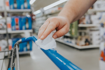 Wall Mural - New normal. Closeup of man hand cleaning shopping cart handle with disinfecting wet wipe. Precaution against virus spread. COVID-19 coronavirus epidemic danger concept.