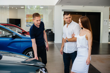 A young couple chooses a new car at the dealership and consults with a representative of the dealership. Used cars for sale. Dream fulfillment