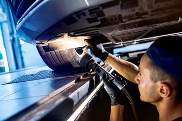 Wall Mural - Car mechanic examining car suspension of lifted automobile at service station