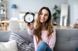 © BestForYou - Young woman showing alarm clock at home.