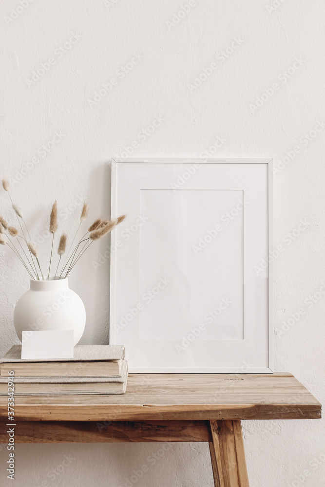 Portrait white picture frame mockup on vintage bench, table. Modern ceramic vase with dry Lagurus ovatus grass, books and busines card. White wall background. Scandinavian interior. Vertical. - obrazy, fototapety, plakaty 