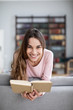 © BestForYou - Attractive young woman is reading a book, looking at camera and smiling.