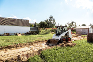 Wall Mural - A skid steer loader clears the site for construction. Land work by the territory improvement. Machine for work in confined areas. Small tractor with a bucket for moving soil and bulk materials.