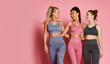 Group of three sport girls international friends posing on pink background. Sporty young women in green and purple